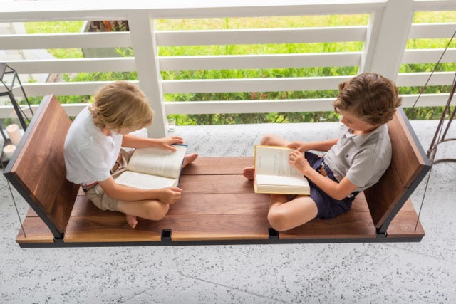 Two boys reading on a modern wooden porch swing