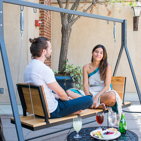 A couple having drinks on a modern wooden porch swing